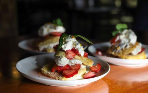 Three plates of strawberry shortcake topped with whipped cream and mint leaves, set on a wooden table.