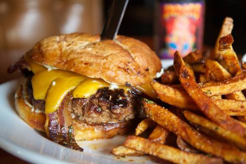 A juicy cheeseburger with melted cheese and crispy bacon, served with a side of golden fries on a white plate.