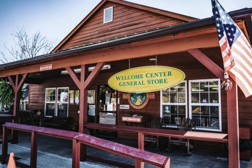 A wooden welcome center and general store with an American flag, featuring a large sign and outdoor seating.