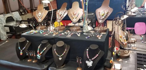 A display of colorful handmade necklaces on stands and tables at a craft fair.