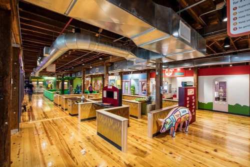 A colorful indoor space with interactive exhibits, wooden floors, and metal ductwork, designed for educational activities.