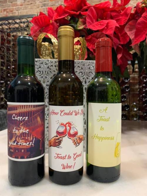 Three wine bottles with festive labels: "Cheers to the Good Times," "How Could We Not Toast to Good Wine," and "A Toast to Happiness."
