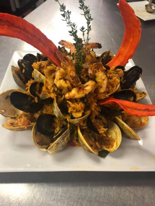A vibrant seafood dish featuring shrimp, mussels, clams, and rice, garnished with red peppers and fresh thyme.