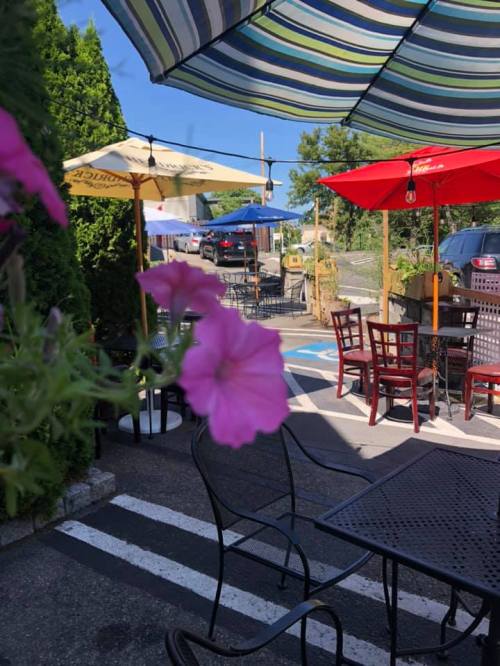 Outdoor dining area with colorful umbrellas, tables, and blooming flowers in a sunny setting.