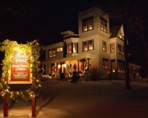 A beautifully lit white house at night, adorned with holiday decorations and a sign for "Stanley Avenue."