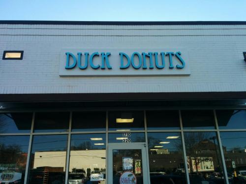 Sign for "Duck Donuts" on a storefront, with a clear blue sky in the background. The shop is open for business.