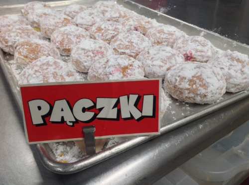 A tray of powdered paczki donuts with a bright red sign displaying the word "Paczki."