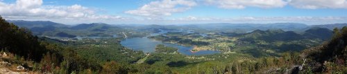 A panoramic view of a lush landscape with lakes, mountains, and a clear blue sky dotted with clouds.