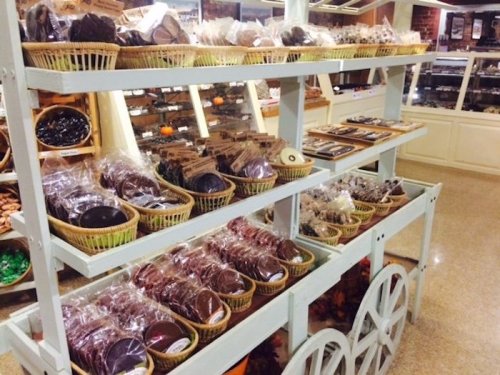 A display of assorted packaged cookies and chocolates on wooden shelves in a cozy shop setting.