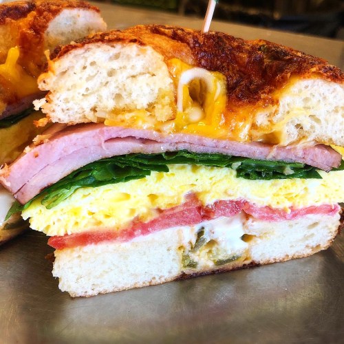 A cross-section of a sandwich with layers of ham, spinach, egg, and melted cheese on a toasted bun.