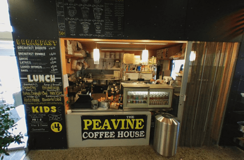 A cozy coffee shop counter with a menu board, drinks, and food items displayed in a casual setting.