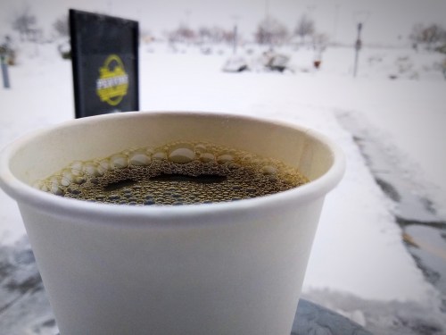 A close-up of a coffee cup with bubbles, set against a snowy outdoor scene.