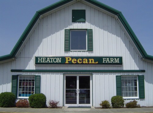 A white barn-style building with green trim, featuring a sign that reads "Heaton Pecan Farm" and an open door.
