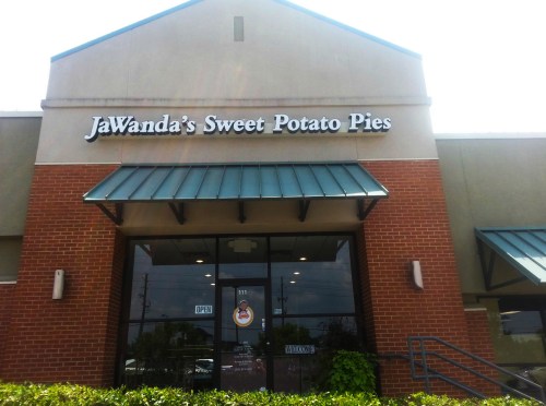 Sign for JaWanda's Sweet Potato Pies on a brick building, featuring an open sign and green awning.