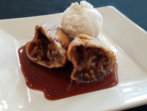 Two fried pastries filled with nuts, drizzled with sauce, served with a scoop of vanilla ice cream on a white plate.