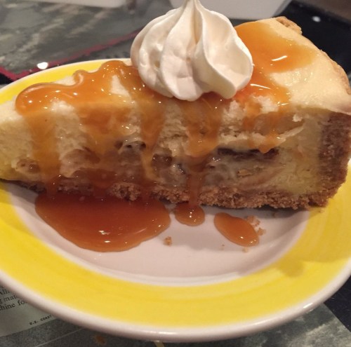 A slice of cheesecake topped with caramel sauce and a dollop of whipped cream on a yellow plate.