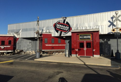 Exterior of the Derailed Diner, featuring a train car and a bold sign, under a clear blue sky.