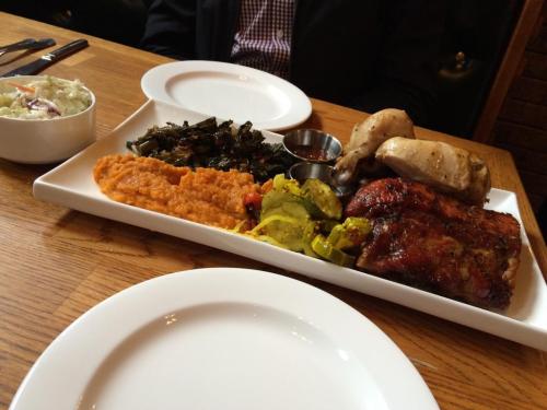 A plate of barbecue ribs, sweet potato mash, collard greens, and grilled vegetables, with a side of coleslaw.