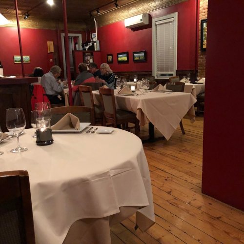 Cozy restaurant interior with red walls, wooden floors, and tables set for dining, featuring patrons in conversation.