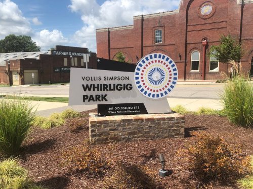 Sign for Vollis Simpson Whirligig Park, featuring a colorful circular design, located at 301 Goldsboro St.