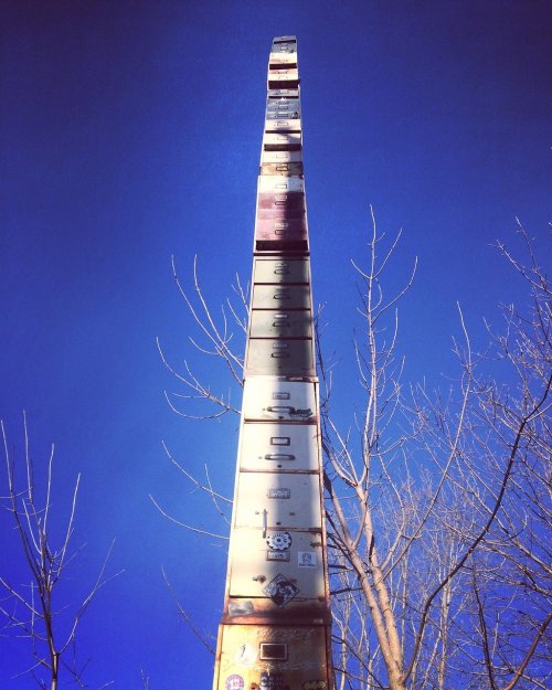A tall, rusted metal structure with drawers, surrounded by bare trees against a clear blue sky.