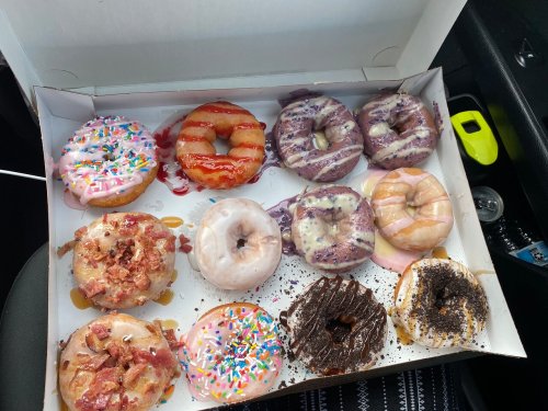 A box of assorted donuts, featuring various toppings like sprinkles, bacon, and glazes, arranged neatly inside.