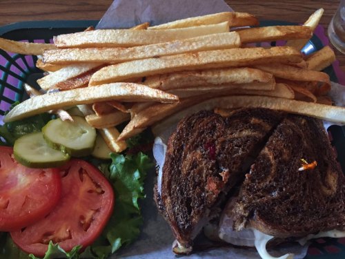 A plate with a sliced sandwich on dark bread, lettuce, tomato, pickles, and a side of golden French fries.
