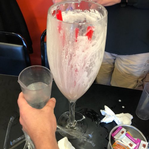 A large, frothy drink in a giant glass with two straws, next to a smaller glass of water on a table.