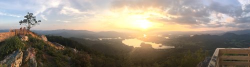 A panoramic view of a sunset over mountains and a lake, with people enjoying the scenery from a lookout point.