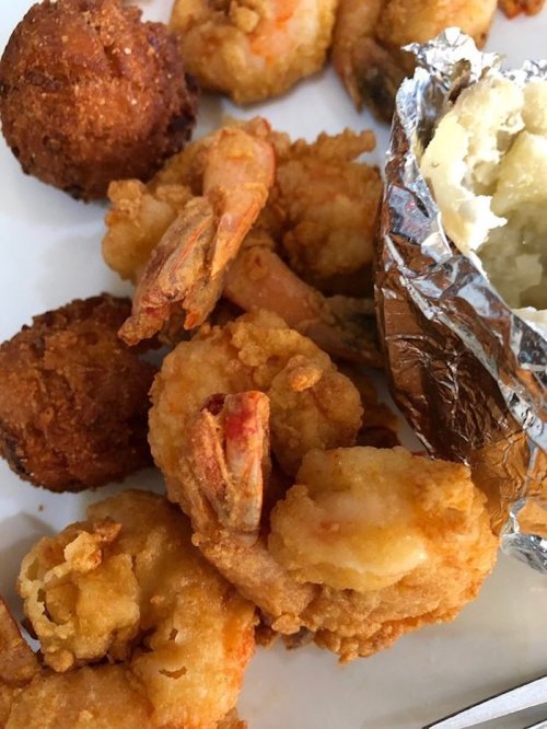 A plate of fried shrimp, hushpuppies, and a baked potato wrapped in foil.