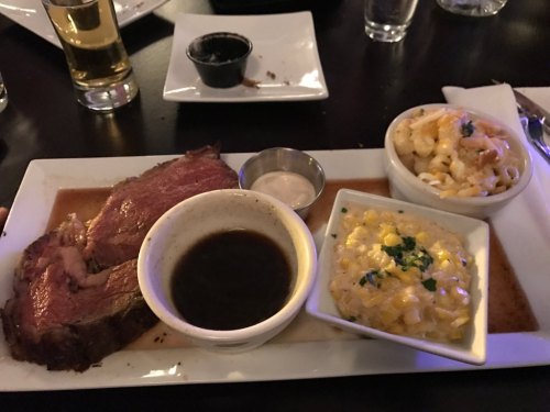 A plate with sliced beef, dipping sauces, and two sides: macaroni and cheese, and corn with herbs.