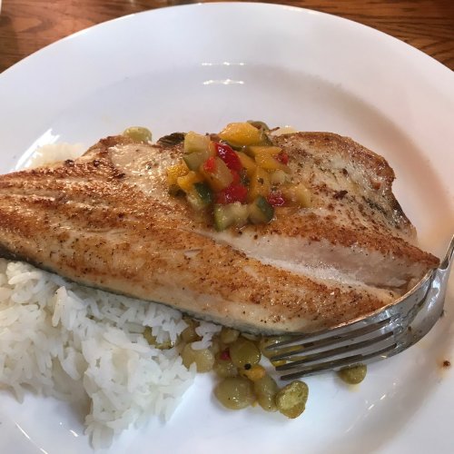 A fillet of grilled fish topped with a colorful salsa, served on a bed of white rice on a white plate.