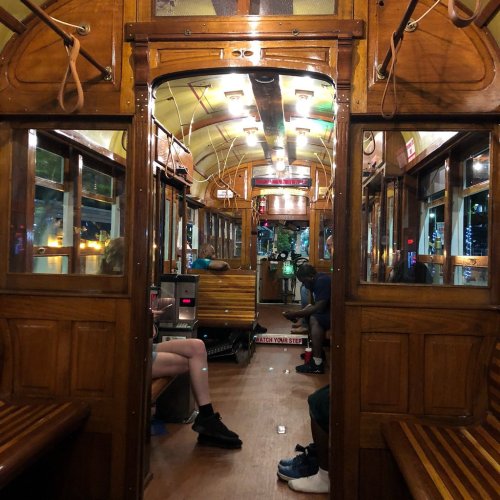Interior of a vintage tram, featuring wooden benches and warm lighting, with passengers seated and a view towards the front.