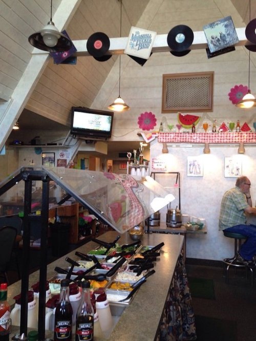 A cozy diner interior with a salad bar, retro decor, and a customer sitting at the counter.