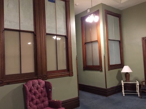 Interior of a room with green walls, large windows, a purple chair, and a lamp on a small table.