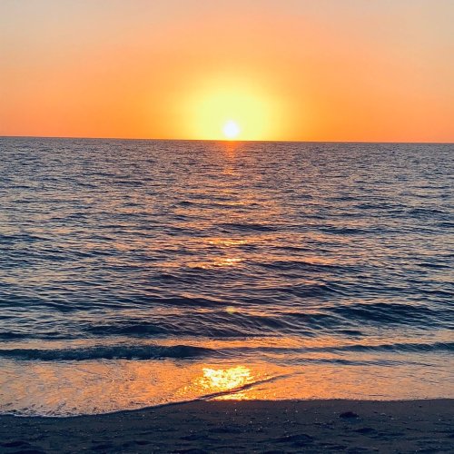 A serene sunset over the ocean, with vibrant orange and yellow hues reflecting on the water's surface.