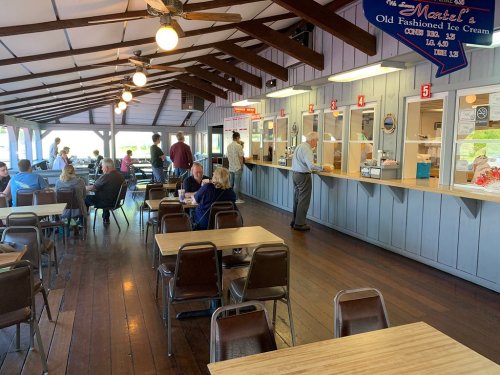A cozy ice cream parlor with wooden tables, patrons enjoying treats, and a service counter in a bright, open space.