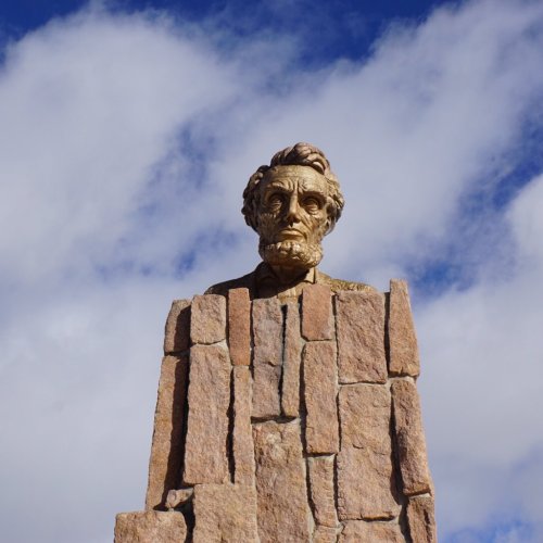 A large stone sculpture of Abraham Lincoln's head against a blue sky with clouds.