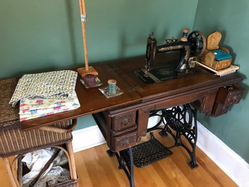 A vintage sewing machine on a wooden table, with fabric, a spool of thread, and a small basket nearby.