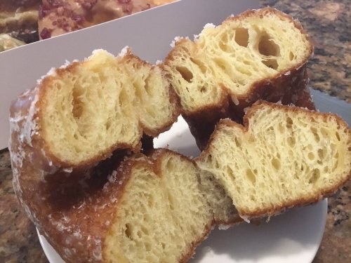 A close-up of a split cronut, showcasing its flaky, airy texture and golden-brown exterior on a plate.
