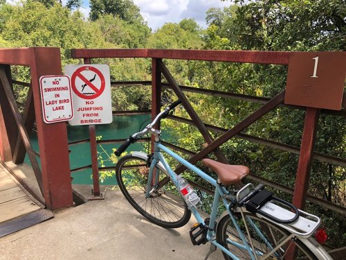 A bike parked on a wooden bridge with signs prohibiting swimming and jumping into the lake below.