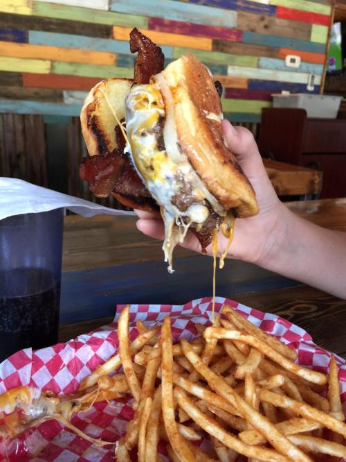 A hand holding a cheesy burger with bacon, dripping with melted cheese, next to a basket of golden fries.