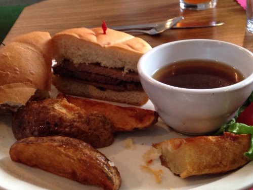 A plate with a sandwich filled with beef, a bowl of gravy, and crispy potato wedges on the side.