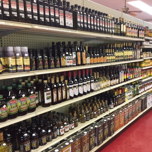A grocery store shelf filled with various bottles of oils, vinegars, and sauces in different sizes and brands.