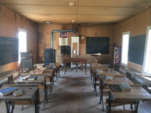A vintage classroom with wooden desks, chalkboards, and a clock, featuring a rustic, worn interior.