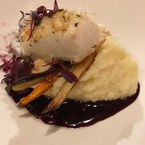 A plated dish featuring fish on creamy mashed potatoes, garnished with colorful vegetables and a dark sauce.