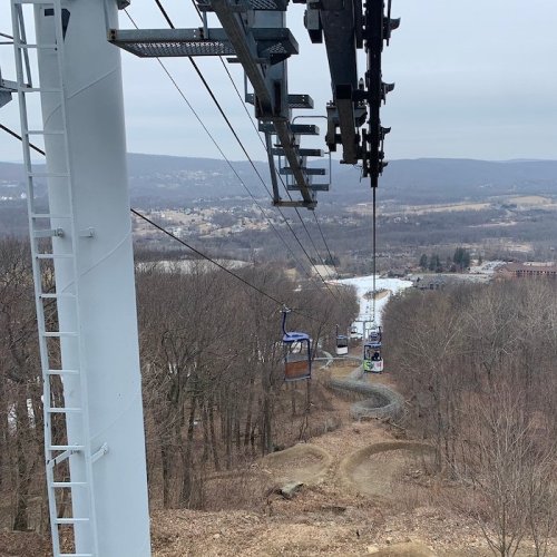 A view from a ski lift overlooking a snowy landscape and distant hills, with empty gondolas descending.
