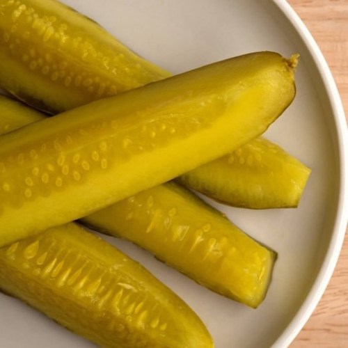 A close-up of several whole pickles arranged on a white plate.
