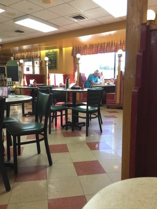 A diner interior with empty tables and a man sitting alone at a table, enjoying a meal in a bright, casual setting.