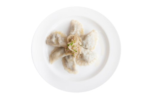 A plate of dumplings arranged in a circular pattern, topped with sautéed onions and garnished with green onions.